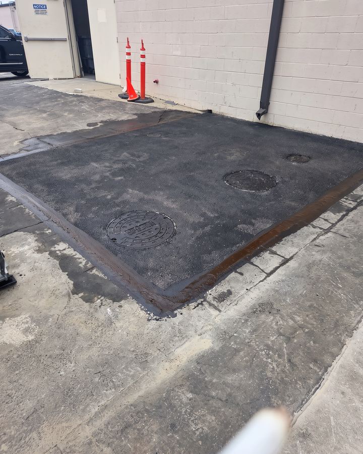 Finished full-depth asphalt patch with cones beside a block wall